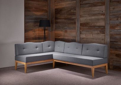 In einem Raum neben einer Holzwand steht eine graue Sofagarnitur mit geschwungener Rückenlehne.