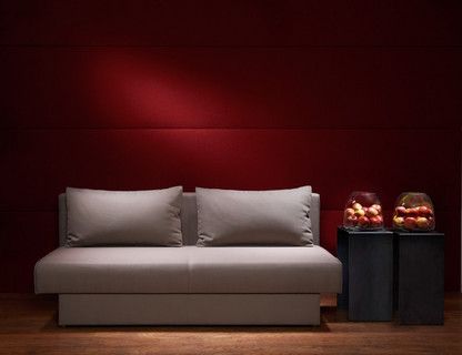 In einem Raum mit Roten Wänden und Holzboden steht ein graues Schlafsofa