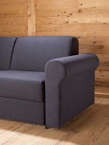 Ein graues Sofa mit runden Armlehnen steht auf einem Holzboden vor einer Holzwand.