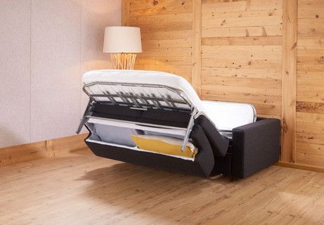 Ein schwarzes ausgeklapptes Sofa steht auf einem Holzboden neben einer Holzwand.