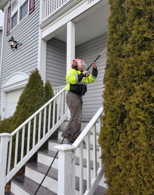 Worker in a neon jacket pressure-washing a house entryway on the front steps