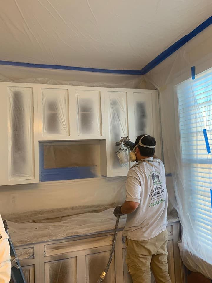 Person spray-painting white cabinet doors in a room, with masked-off walls and countertops.