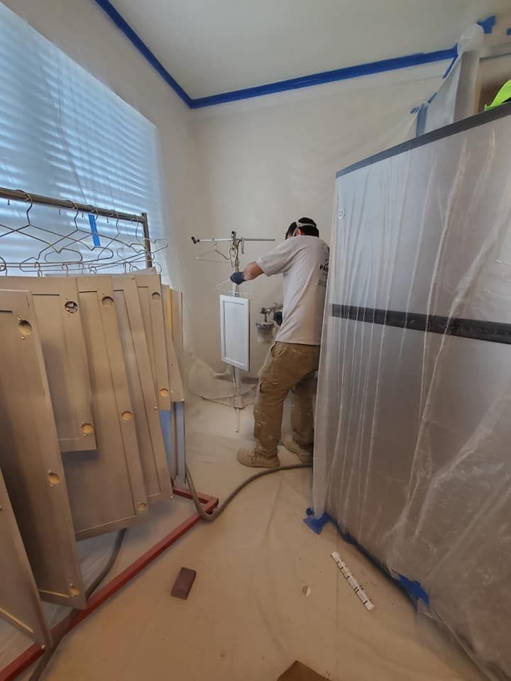 Person spray-painting a cabinet in a taped-off room with plastic-covered furniture