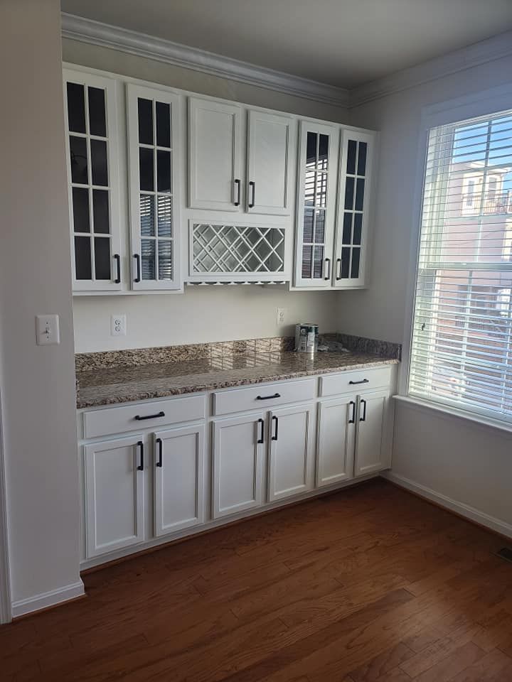 White kitchen cabinets and granite countertop in a bright room with wood floors and a window with blinds