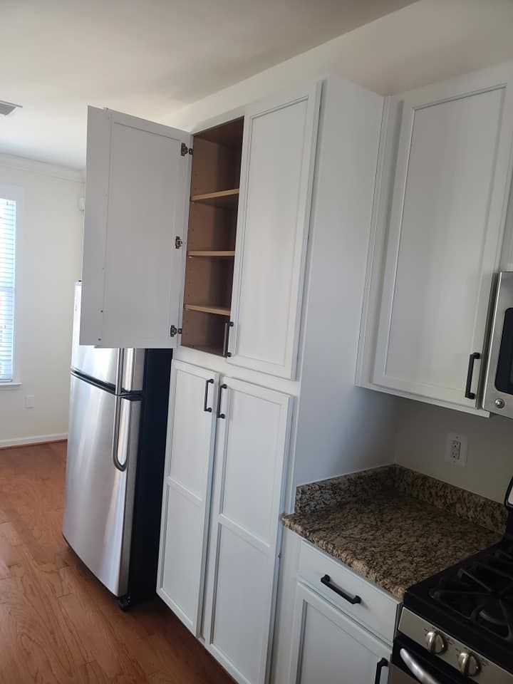 Kitchen with white cabinets, stainless fridge, granite countertop, and open pantry shelves.
