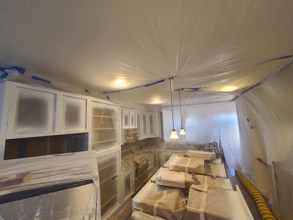 Kitchen under renovation with white cabinets, covered counters, and plastic sheeting protecting the room.