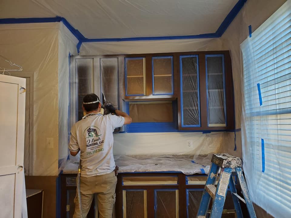Person painting kitchen cabinets in a room with blue trim, white walls, and a ladder nearby.