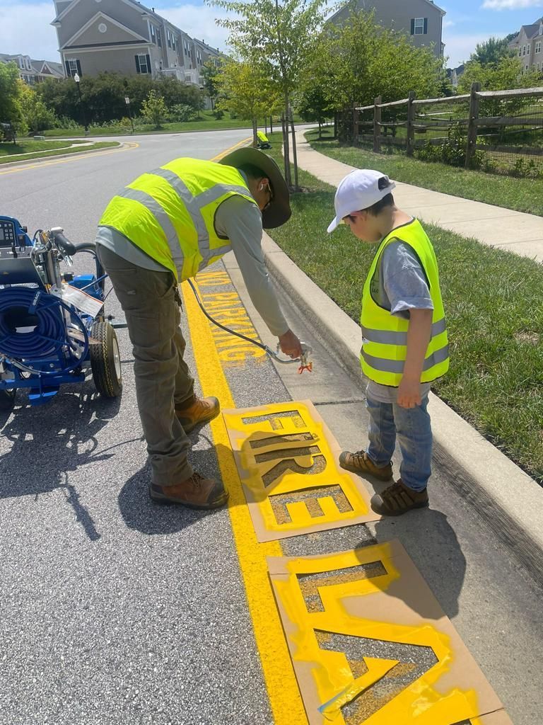 Two people in high-visibility vests use a stencil to paint 