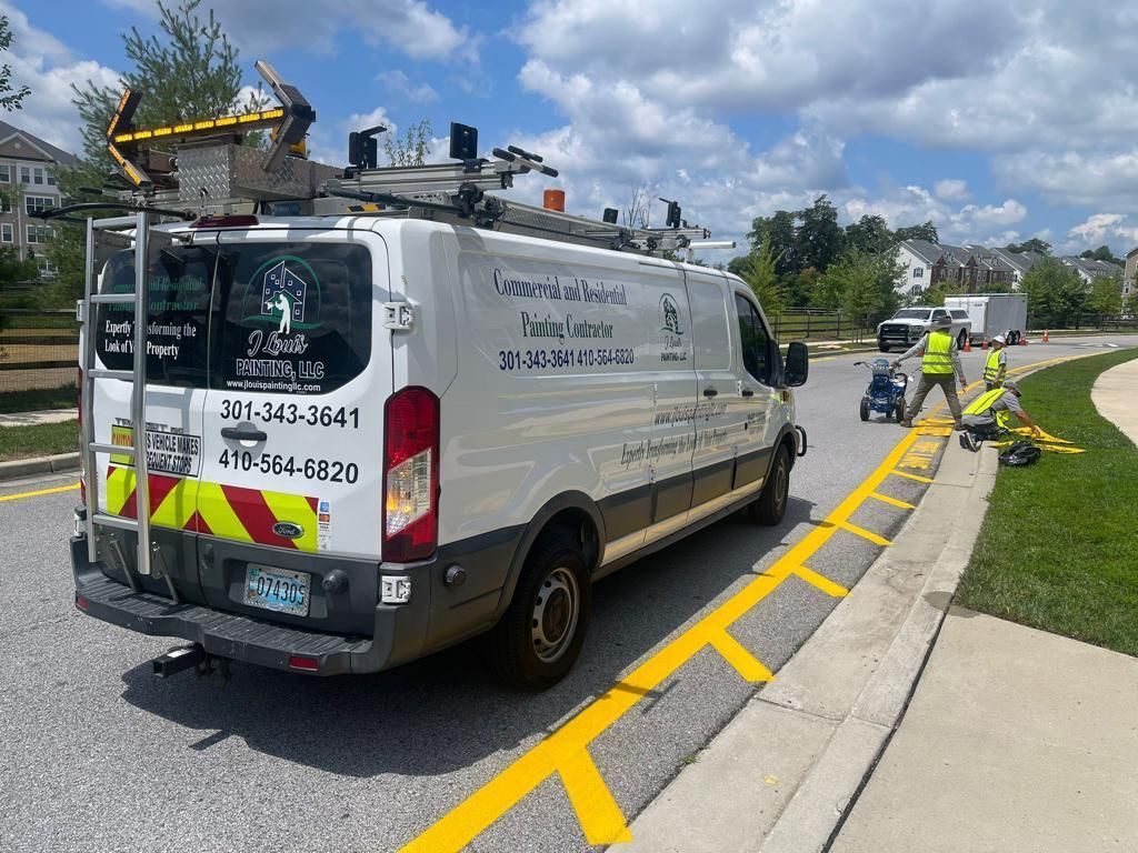White utility van parked on a curb beside a yellow-striped sidewalk, with workers and equipment nearby.