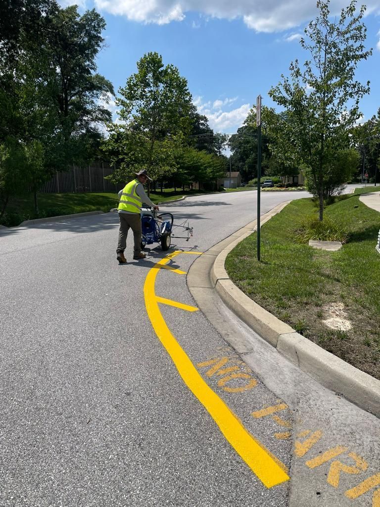 Worker using a line-marking machine painting a yellow road line on a sunny suburban street