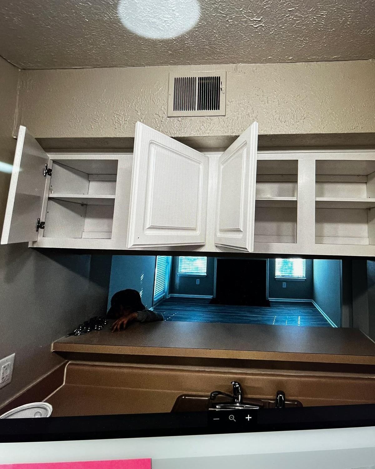 Inside a pantry-like room with open cabinets, a central white door, and a bed or bench below a windowed opening.