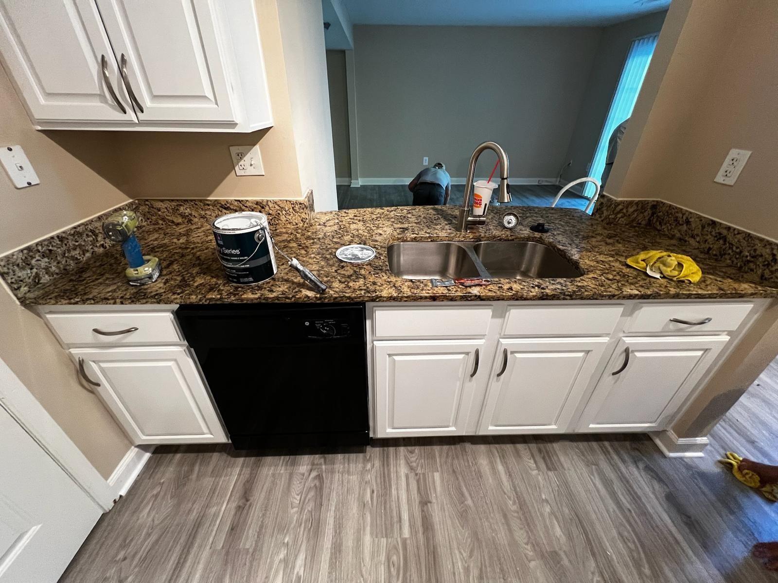 Kitchen counter with granite top, sink, black dishwasher, and white cabinets overlooking a window