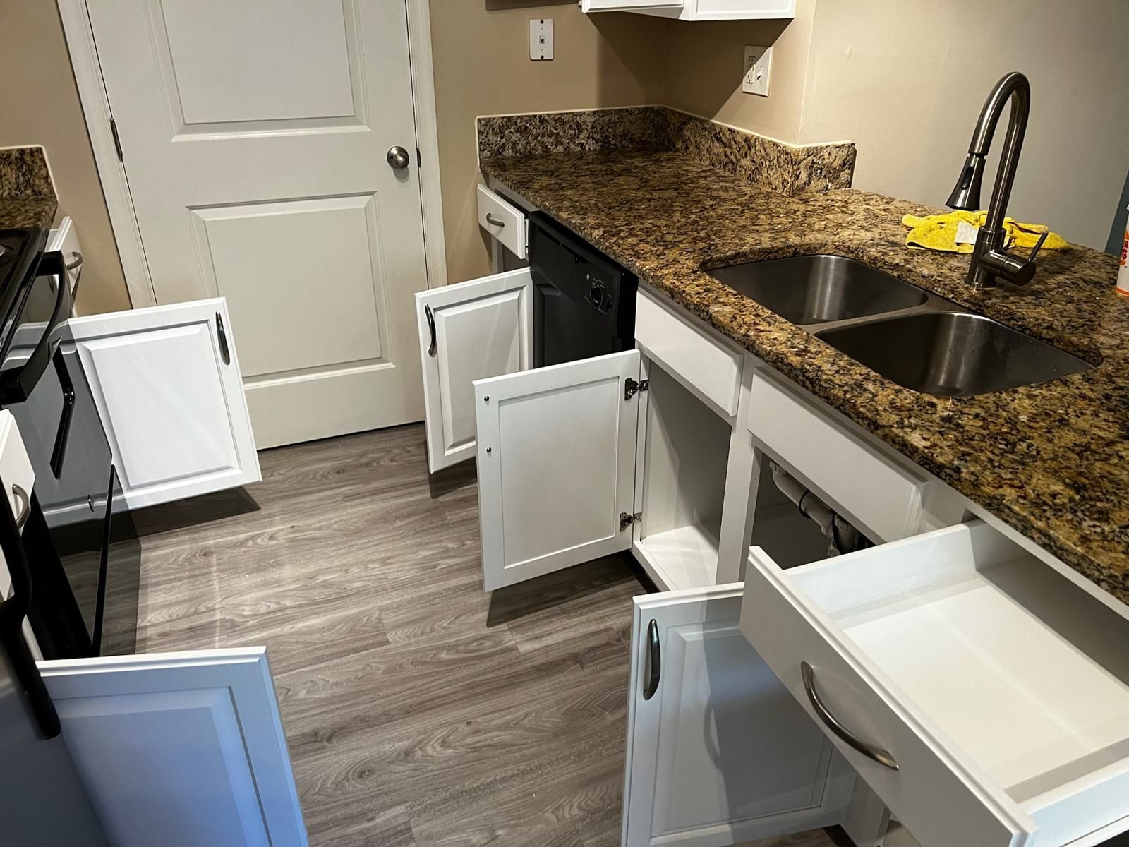 Modern kitchen with open cabinets and drawers, granite counters, black sink, and wood-look flooring