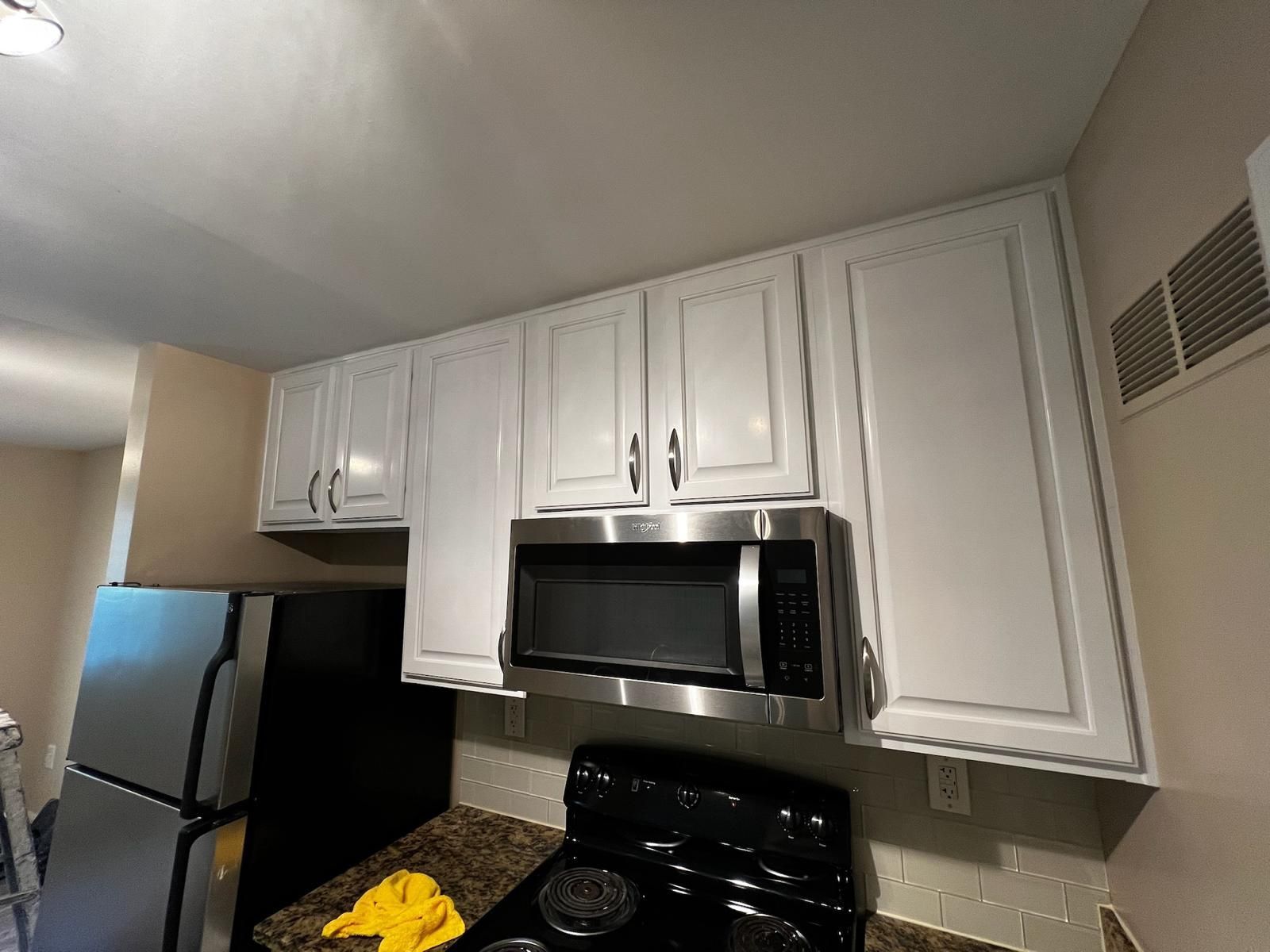 White kitchen cabinets above a black stove and microwave, with a refrigerator on the left.