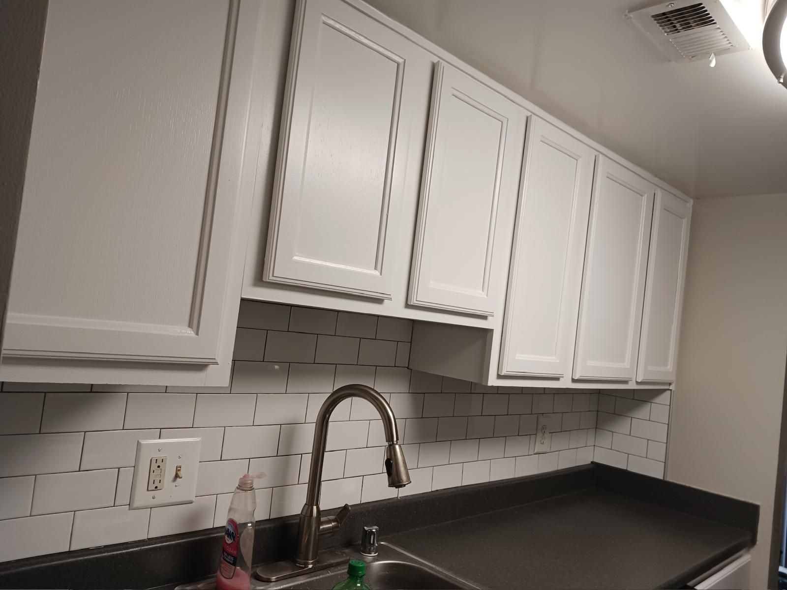 White kitchen cabinets above a black countertop with a sink and chrome faucet under subway tile backsplash