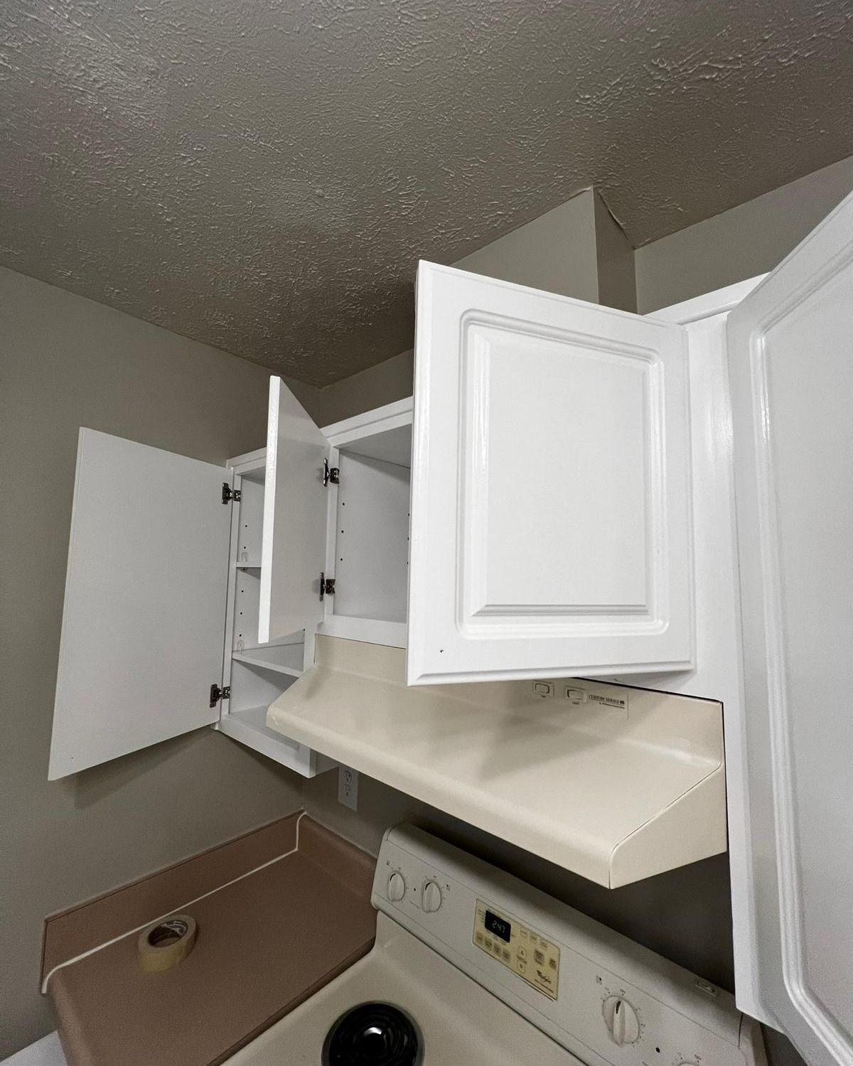 Open kitchen cabinets above a stove and sink, with white doors and one cabinet hanging open.