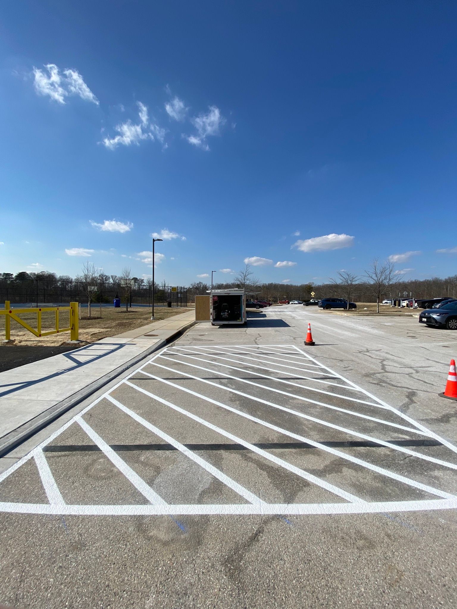 Empty parking lot with diagonal white painted lines, traffic cones, and a blue sky with clouds