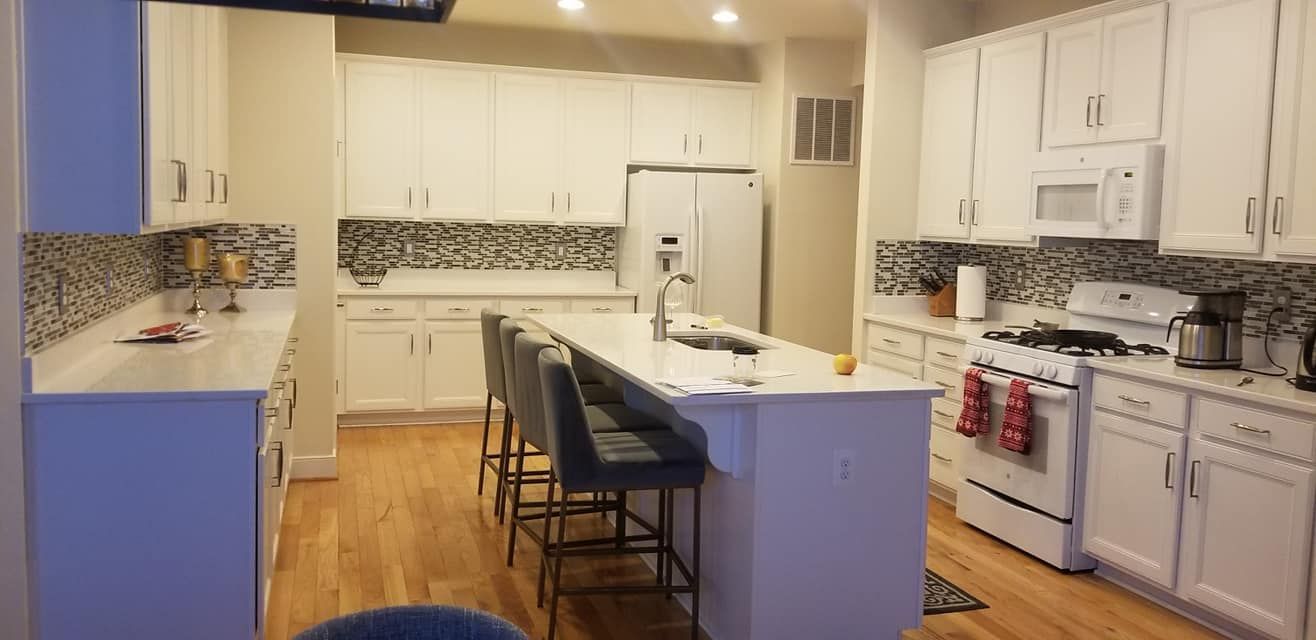Bright modern kitchen with white cabinets, blue island, bar stools, and tiled backsplash