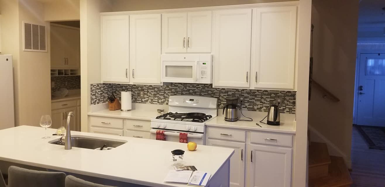 Bright kitchen with white cabinets, stove, microwave, tiled backsplash, and a white island in the foreground