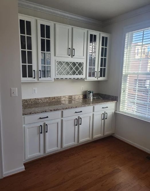 Bright kitchen with white cabinets, granite countertop, wine rack, and a large window beside hardwood floors