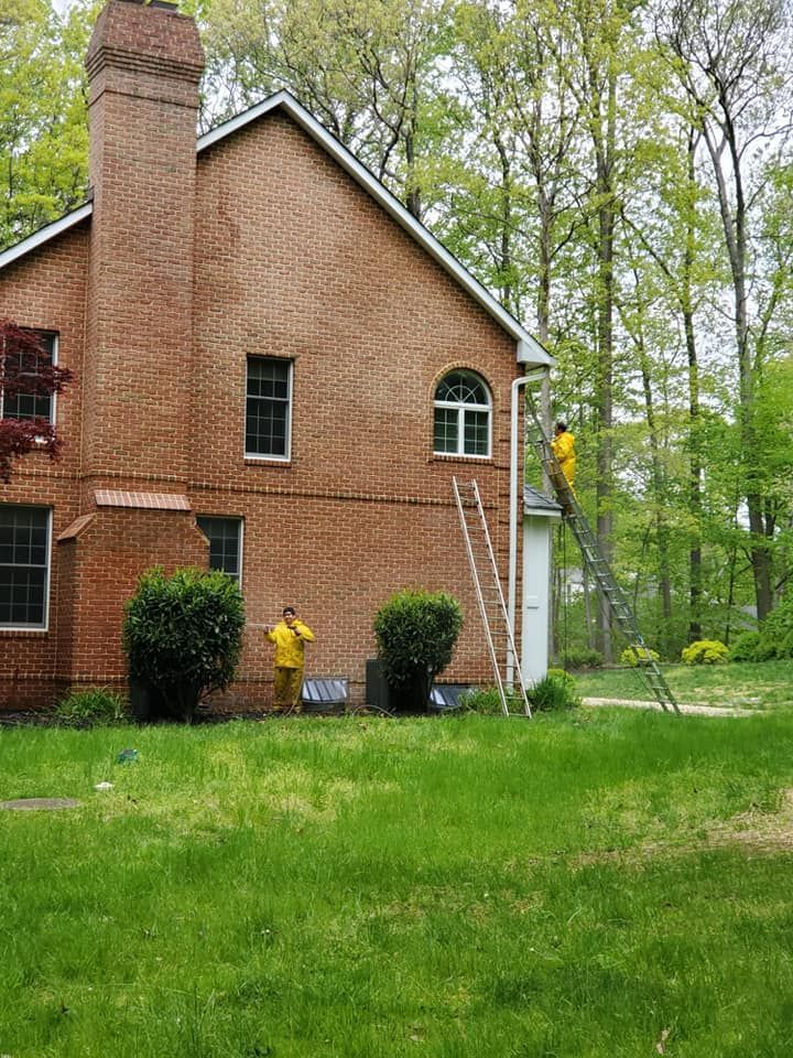 Brick house with chimney and green lawn, surrounded by trees, with a person in a yellow shirt near the wall