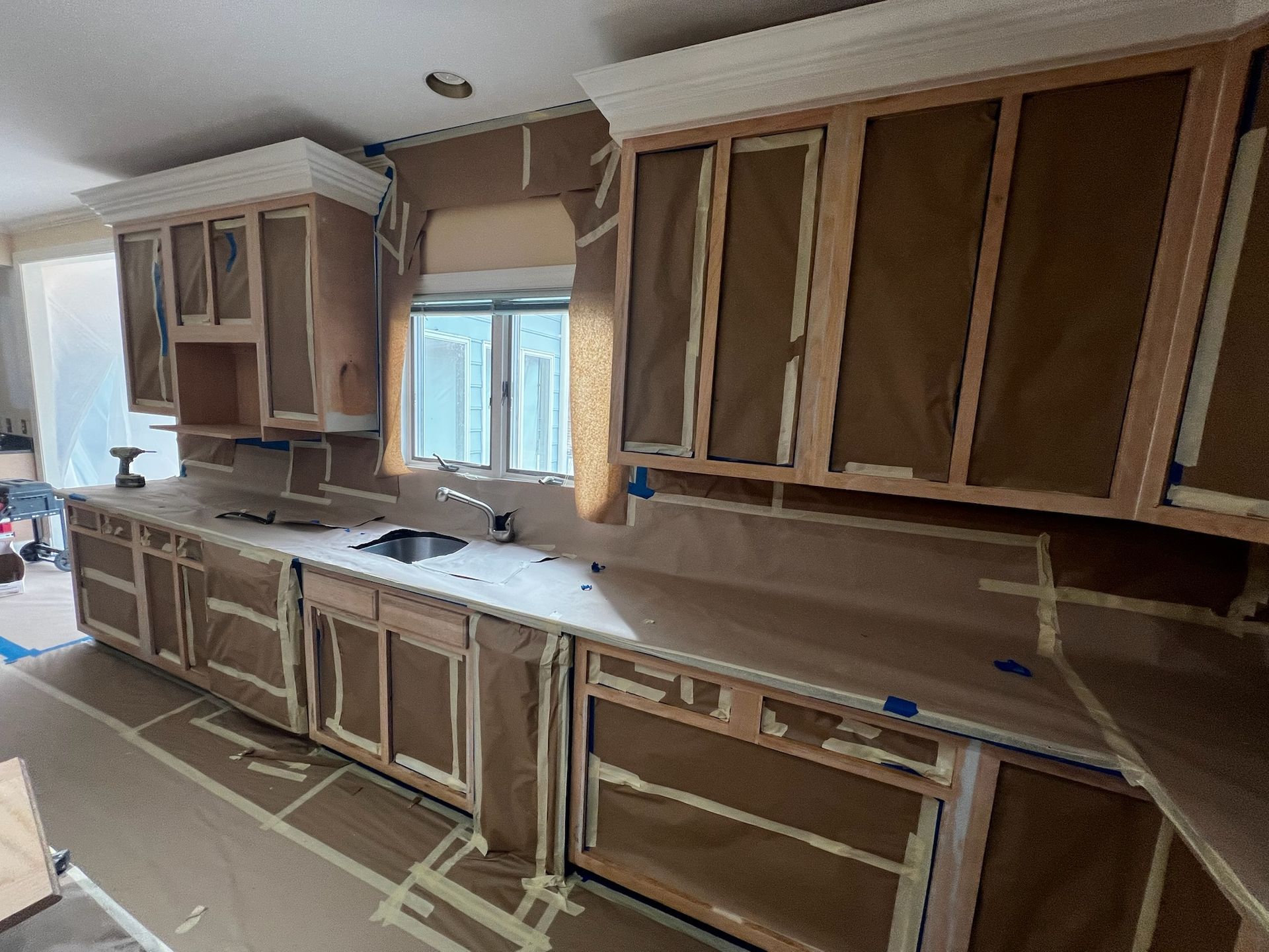 Unfinished kitchen with brown cabinets, covered countertops, and a central window under construction.