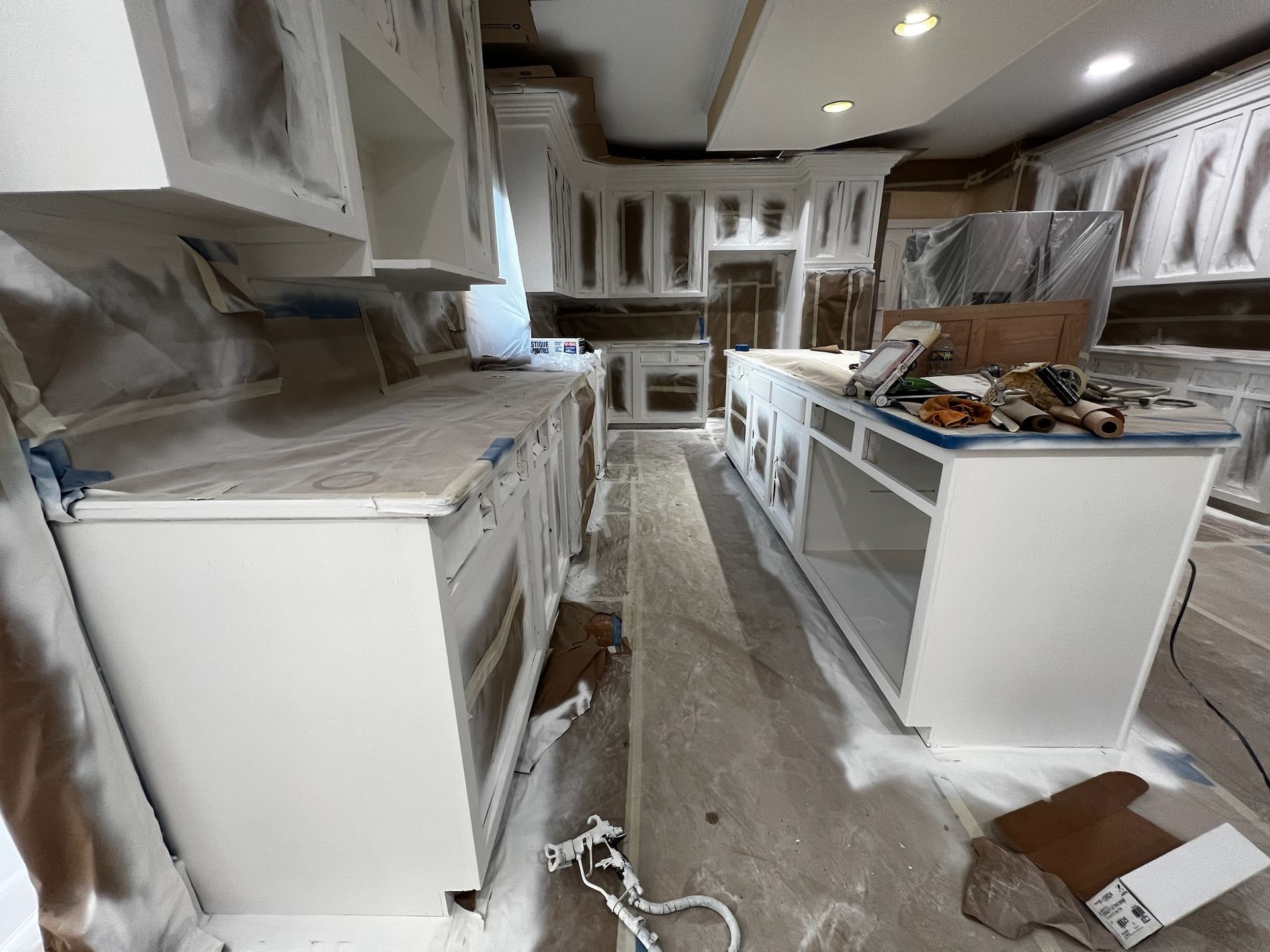 Renovated kitchen with white cabinets, countertops, and tools scattered on the floor and island.