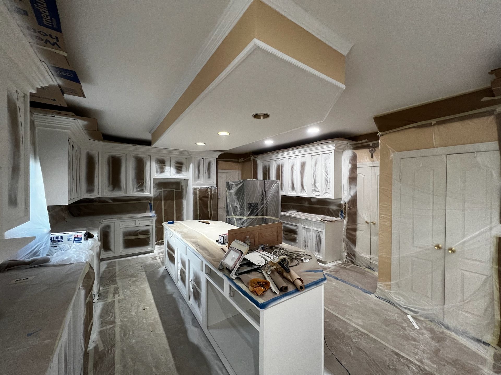 Kitchen under renovation with plastic-covered cabinets, a central island, and ceiling lights on.
