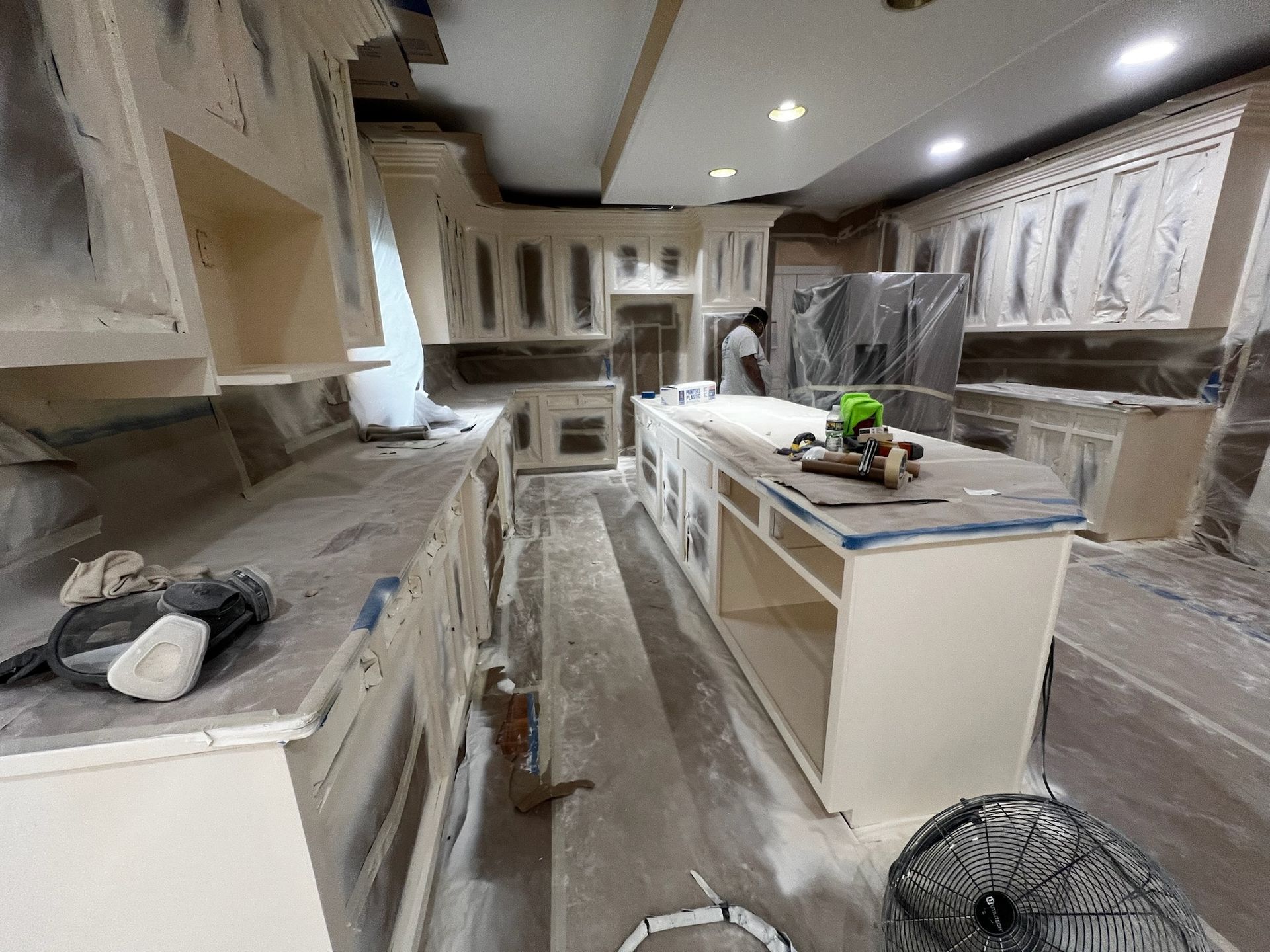 Kitchen under renovation with white cabinets, central island, tools, and construction dust on the floor.