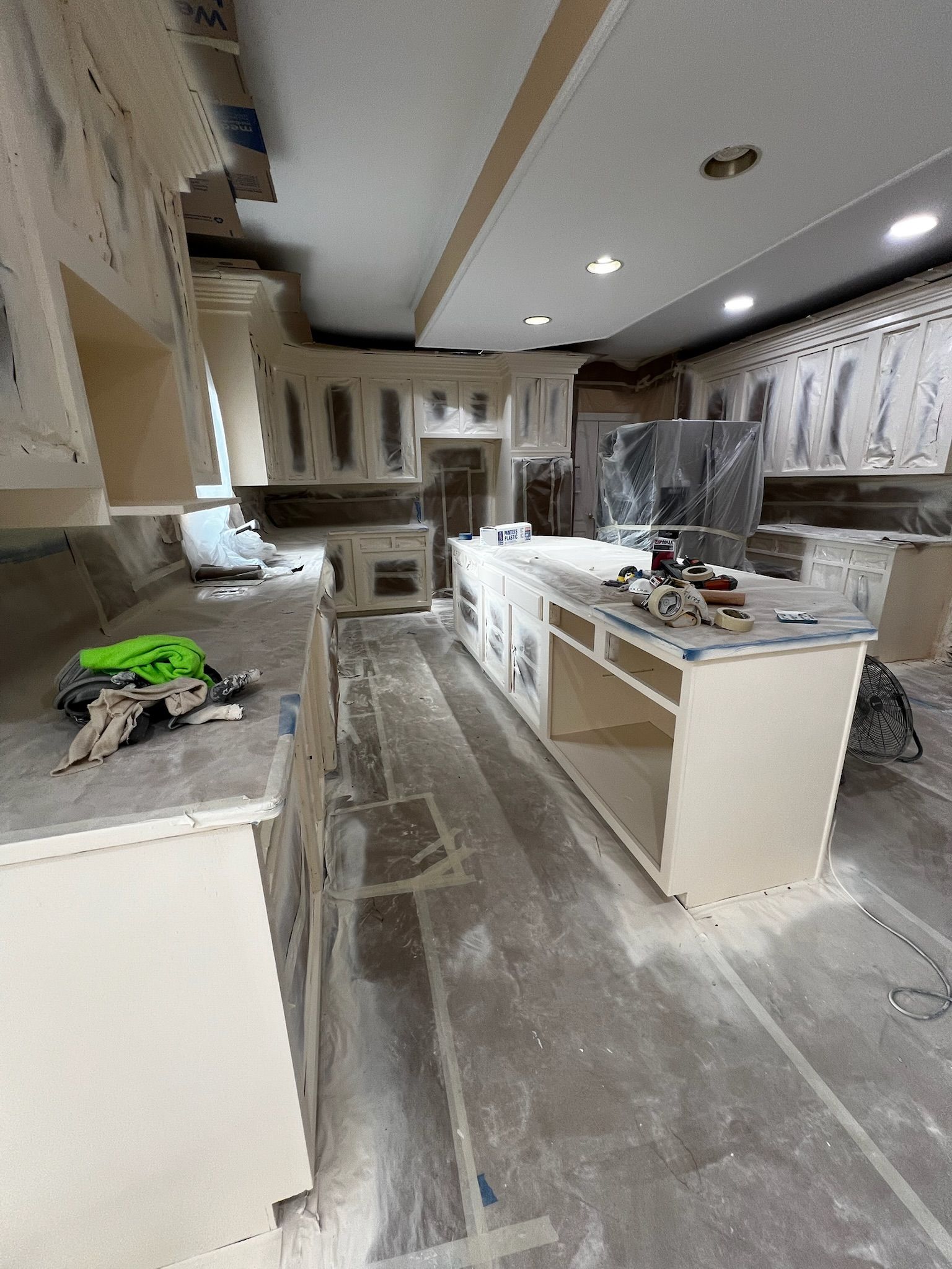 Partially remodeled kitchen with white cabinets, gray countertops, and construction materials on the floor