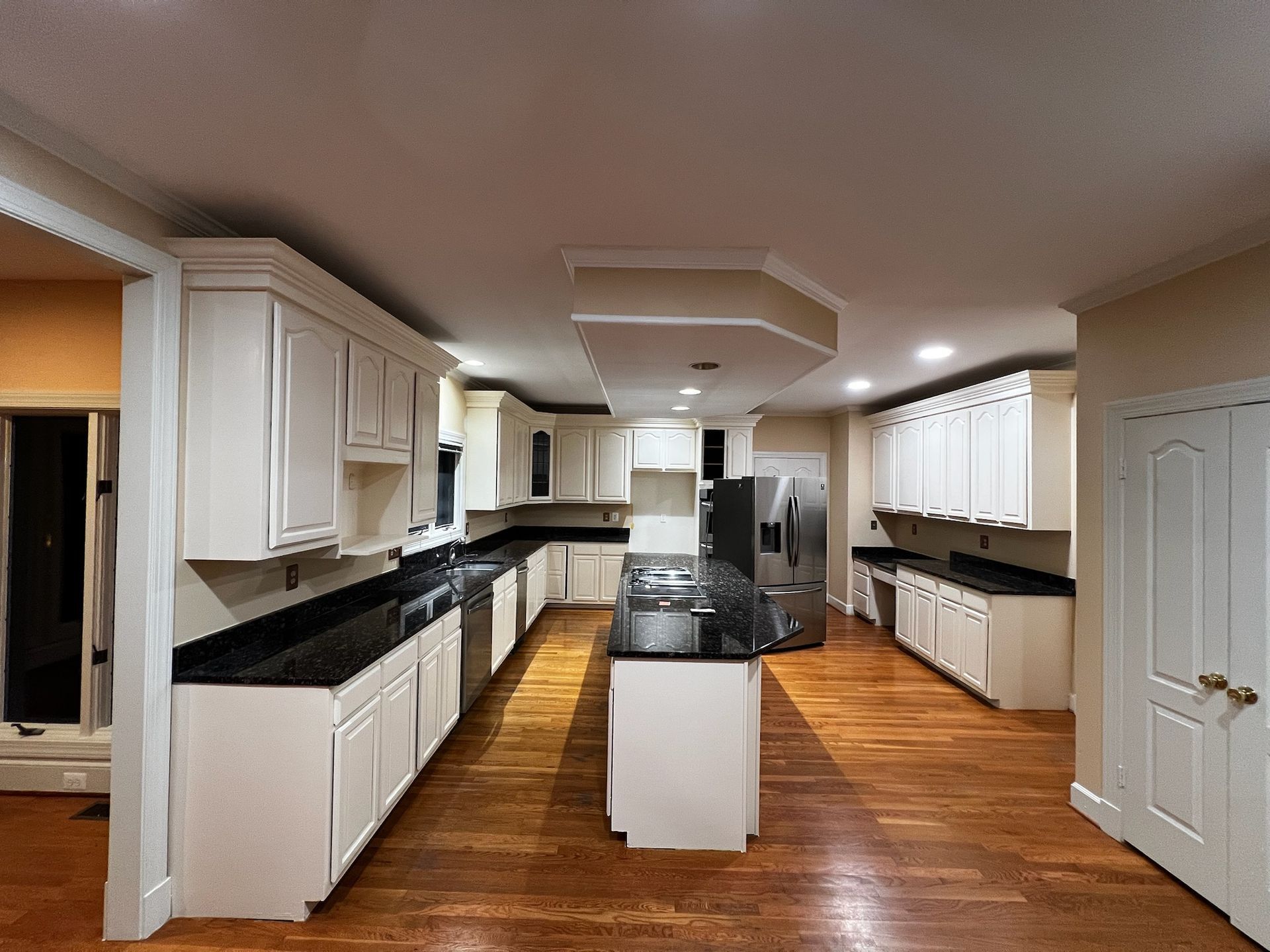 Bright kitchen with white cabinets, black countertops, and a central island on wood flooring.