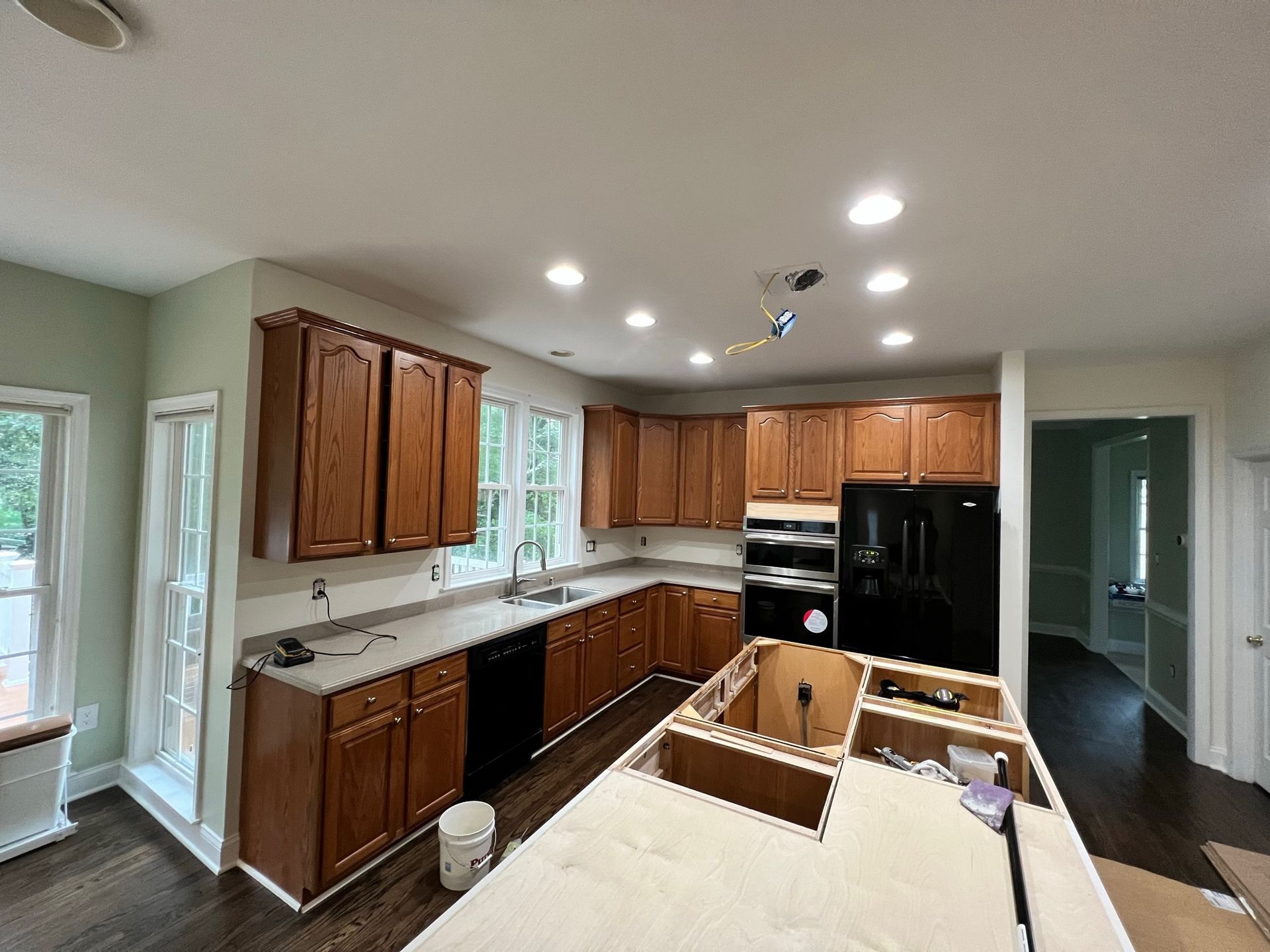 Kitchen with wooden cabinets, white countertops, black appliances, and a partially built island on a dark floor.