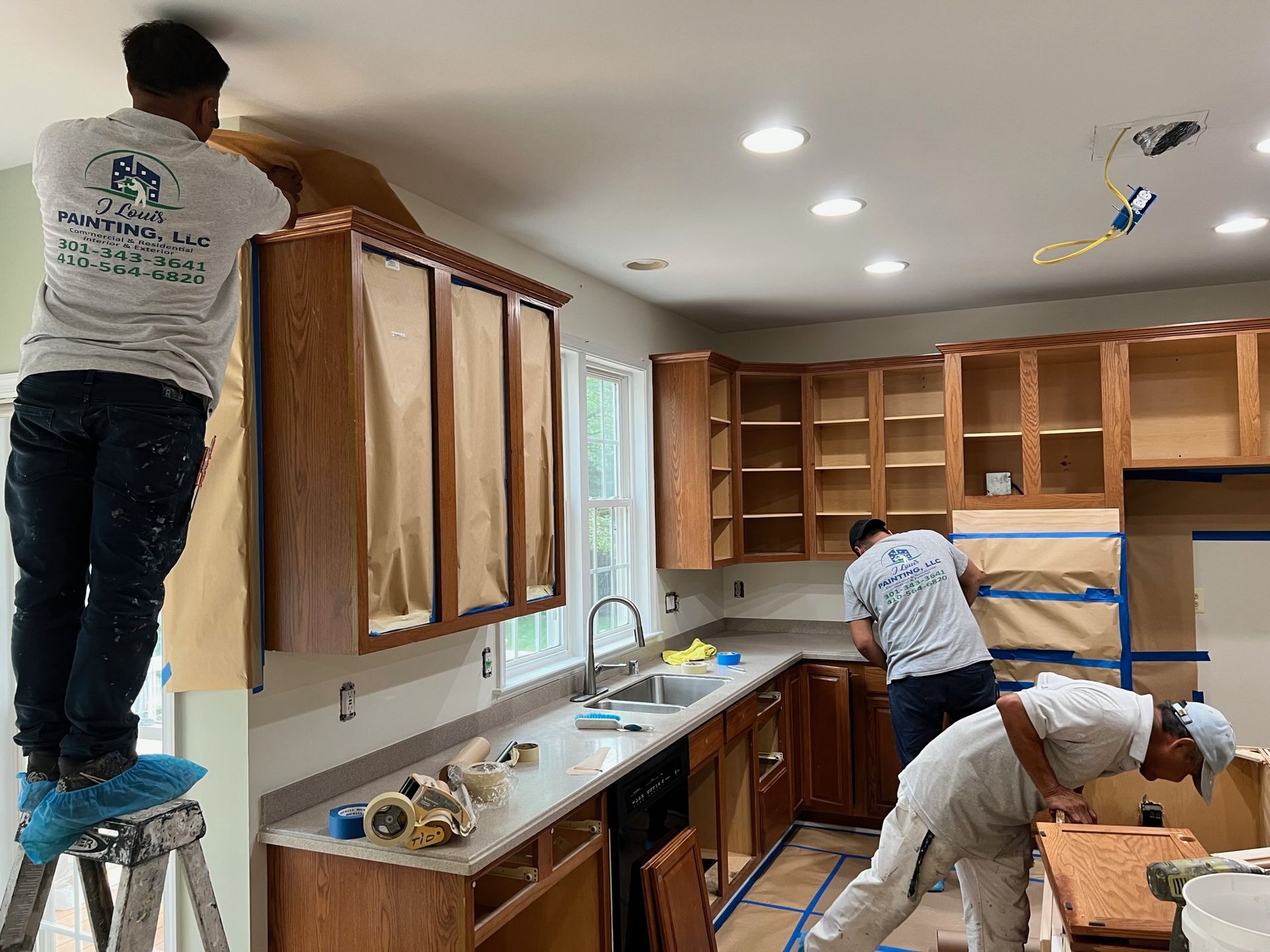 Workers installing kitchen cabinets in a bright, unfinished kitchen with open wood cabinets and tools on the counter