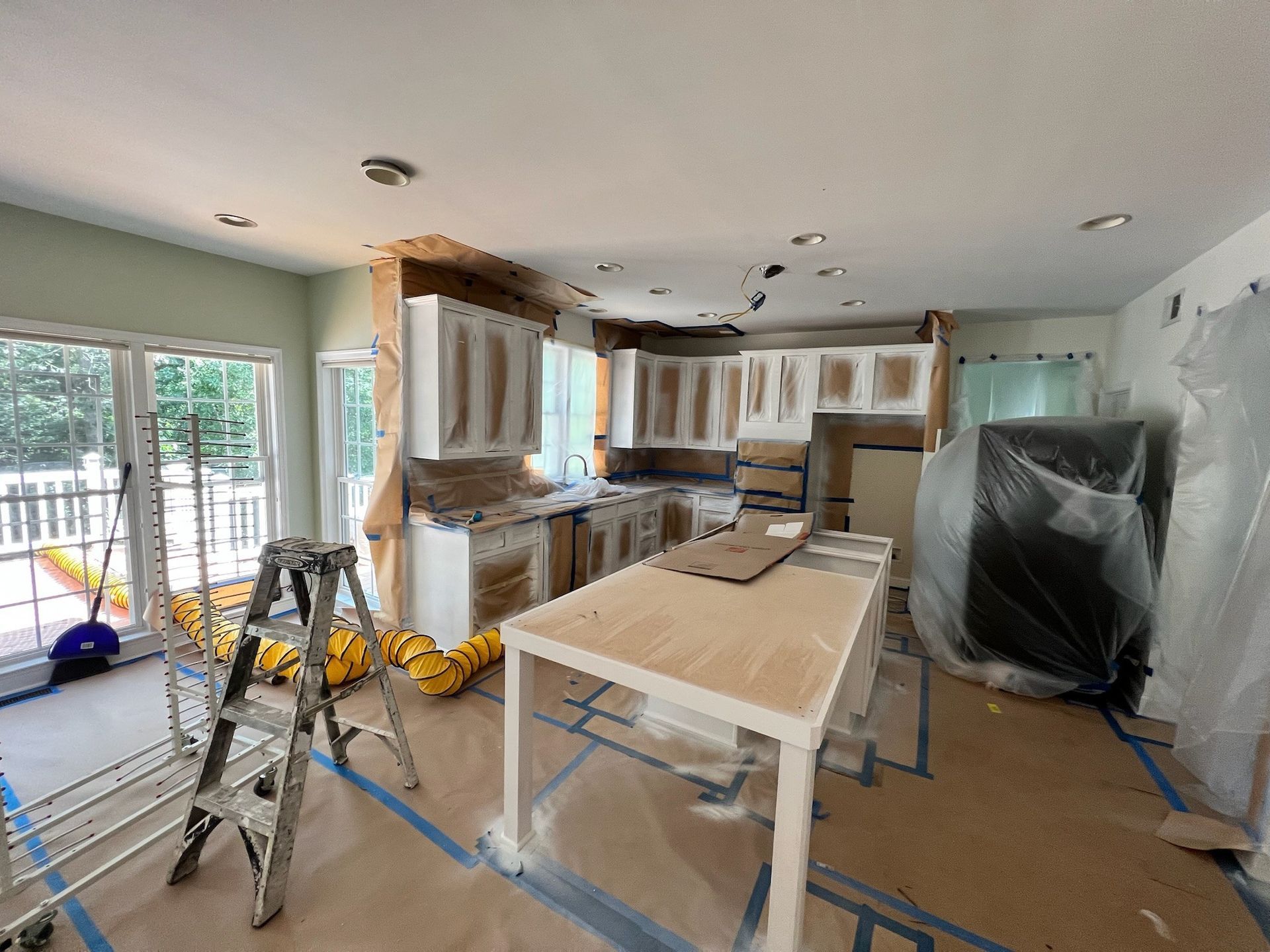 Kitchen under renovation with covered cabinets, ladders, and a work table over protected floors
