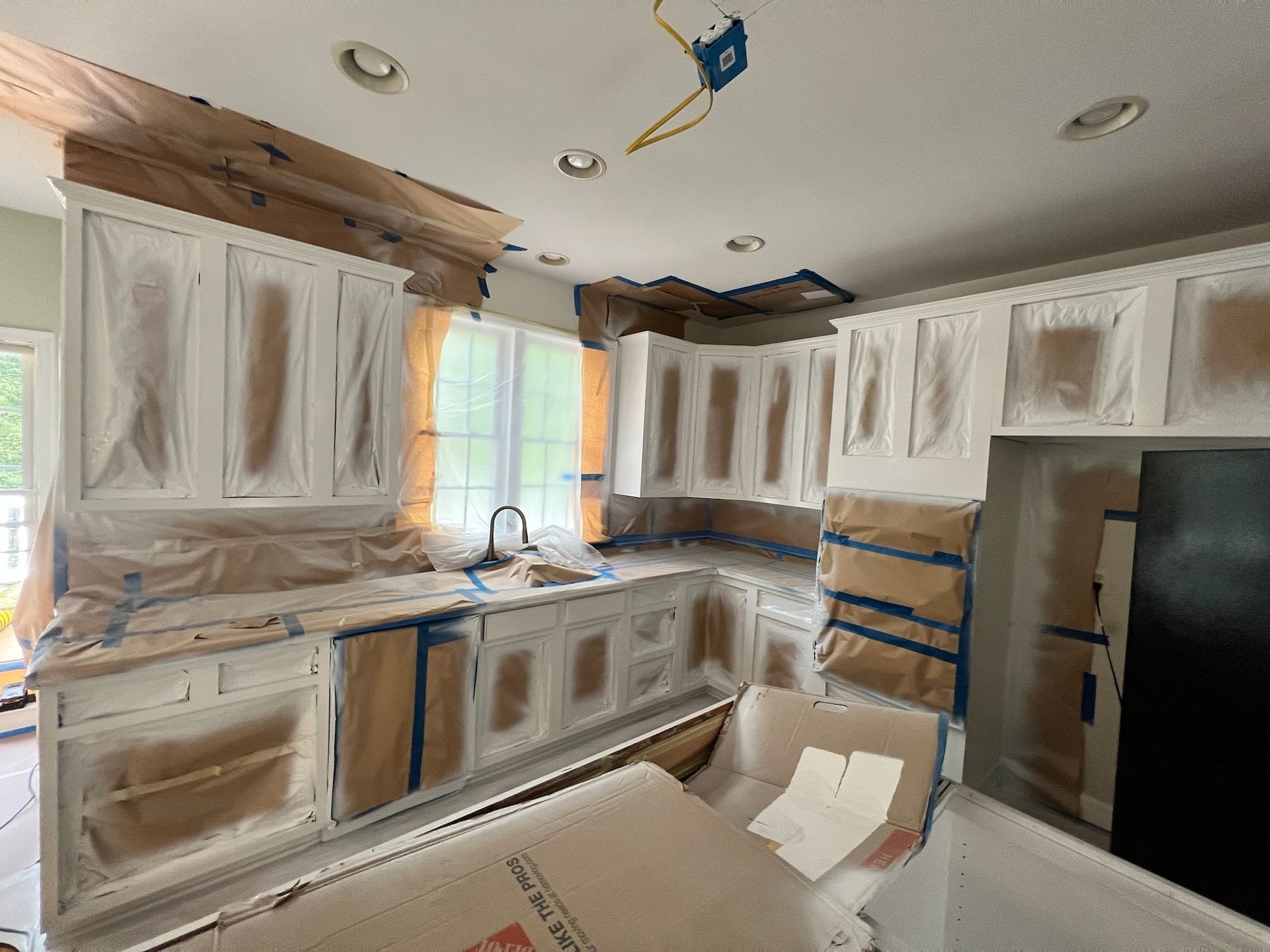 Kitchen under renovation with white cabinets taped off and covered for painting