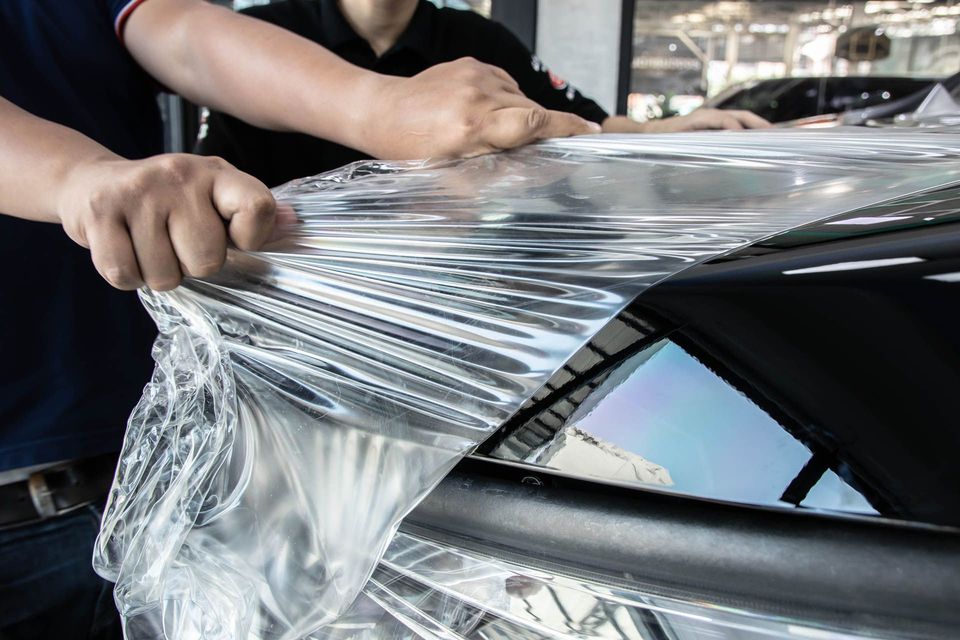 Hands stretching clear vinyl wrap over a glossy black car - Window Tint and Paint Film Protection in Ocala, FL