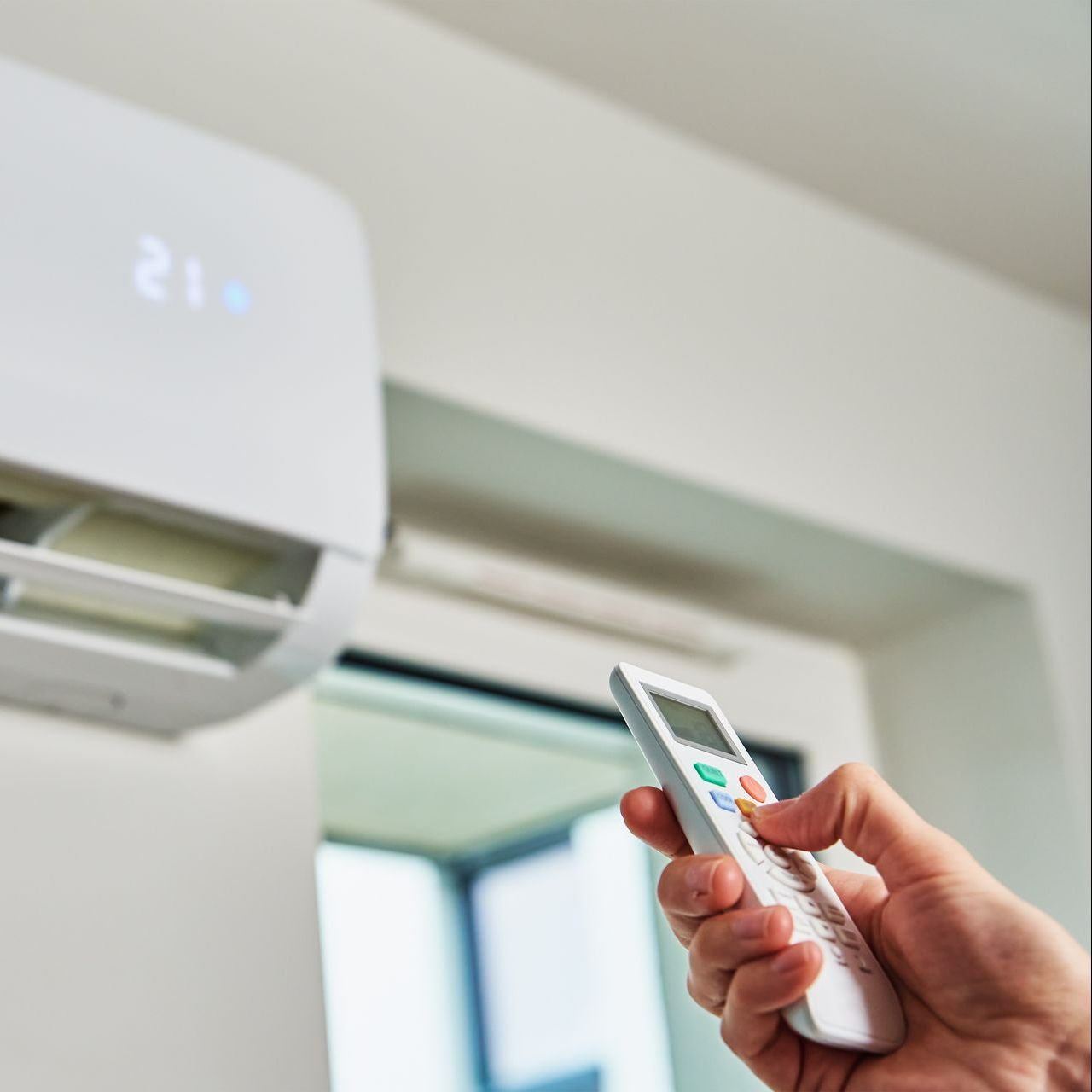A person is holding a remote control in front of an air conditioner.