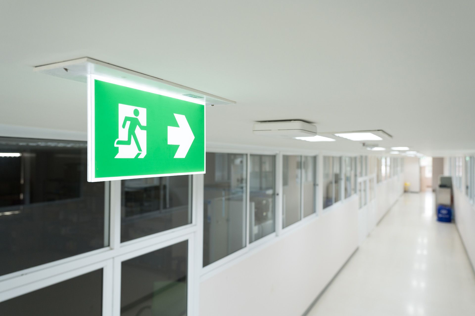 A hospital hallway with a green exit sign hanging from the ceiling.