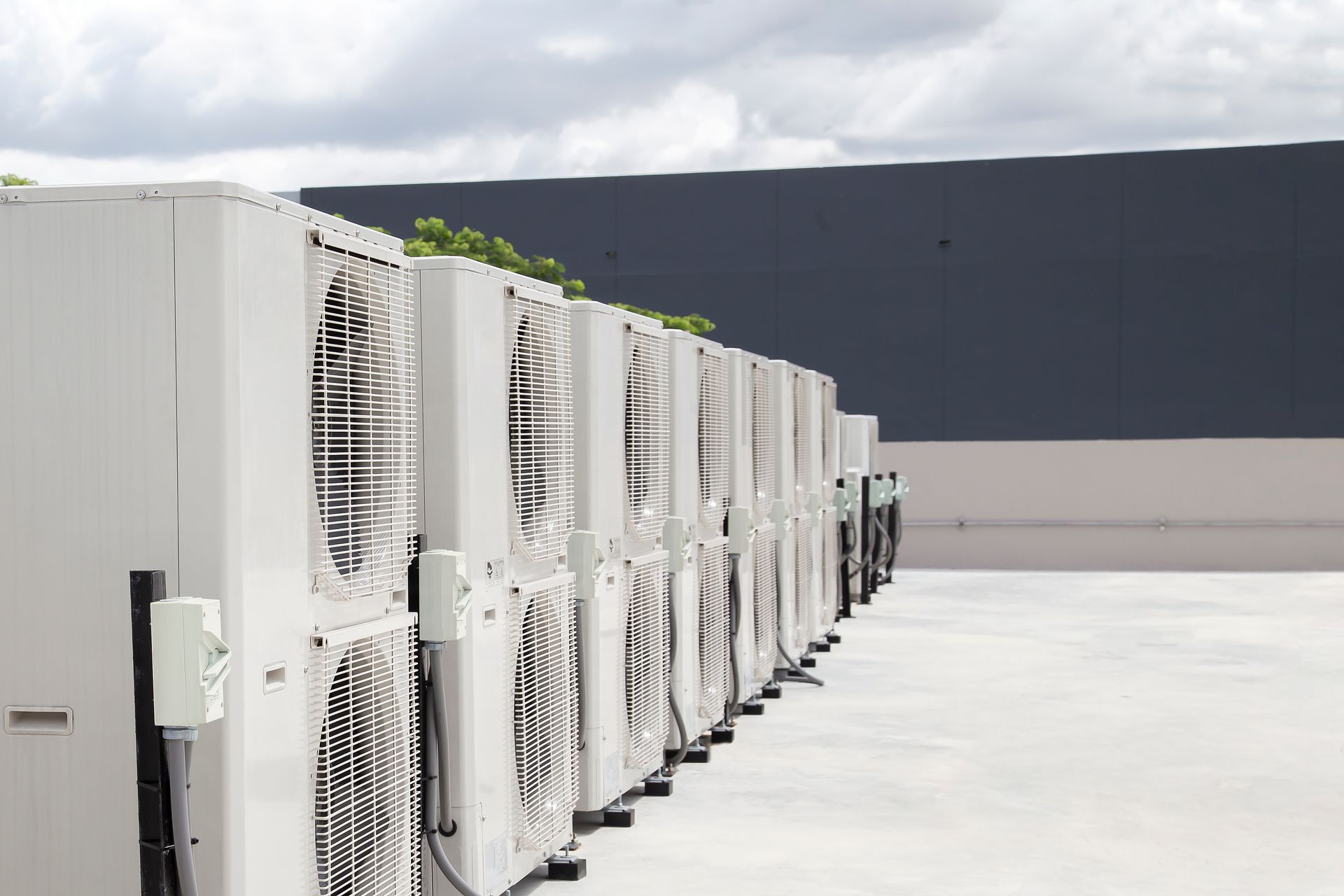 A row of air conditioners are lined up on the side of a building.