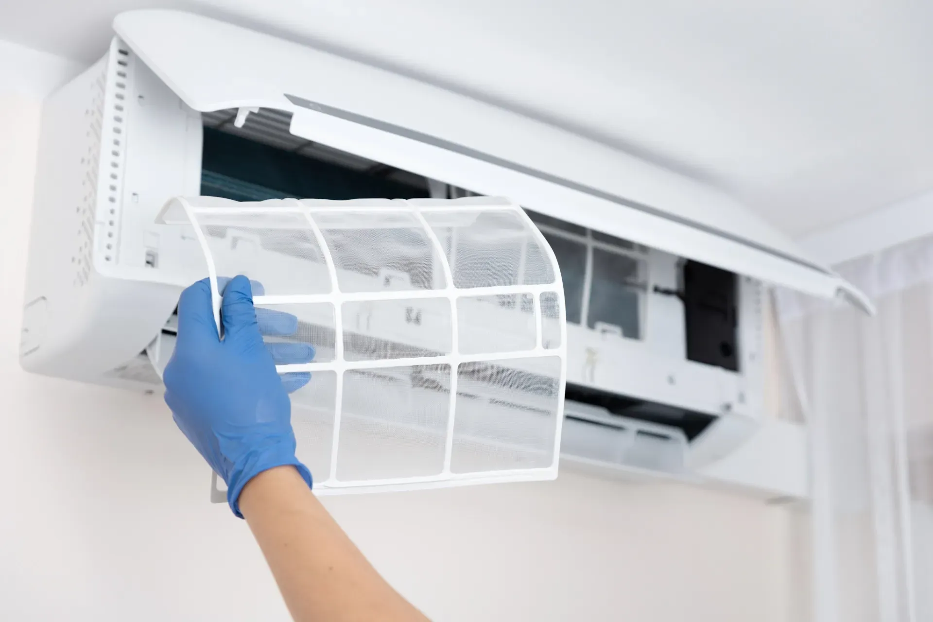 A person wearing blue gloves is cleaning an air conditioner.
