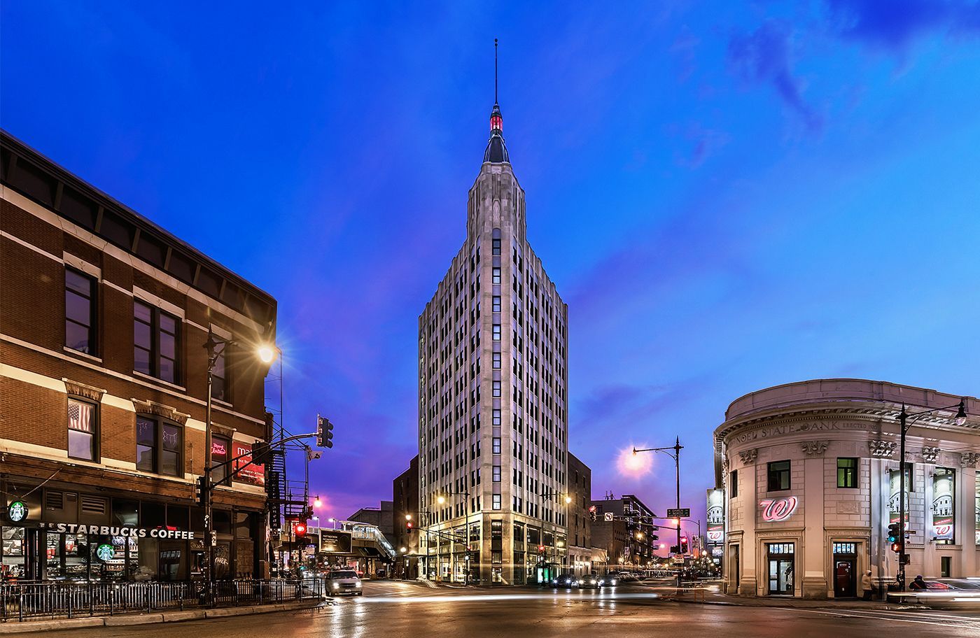 A large building is sitting on the corner of a city street at night.
