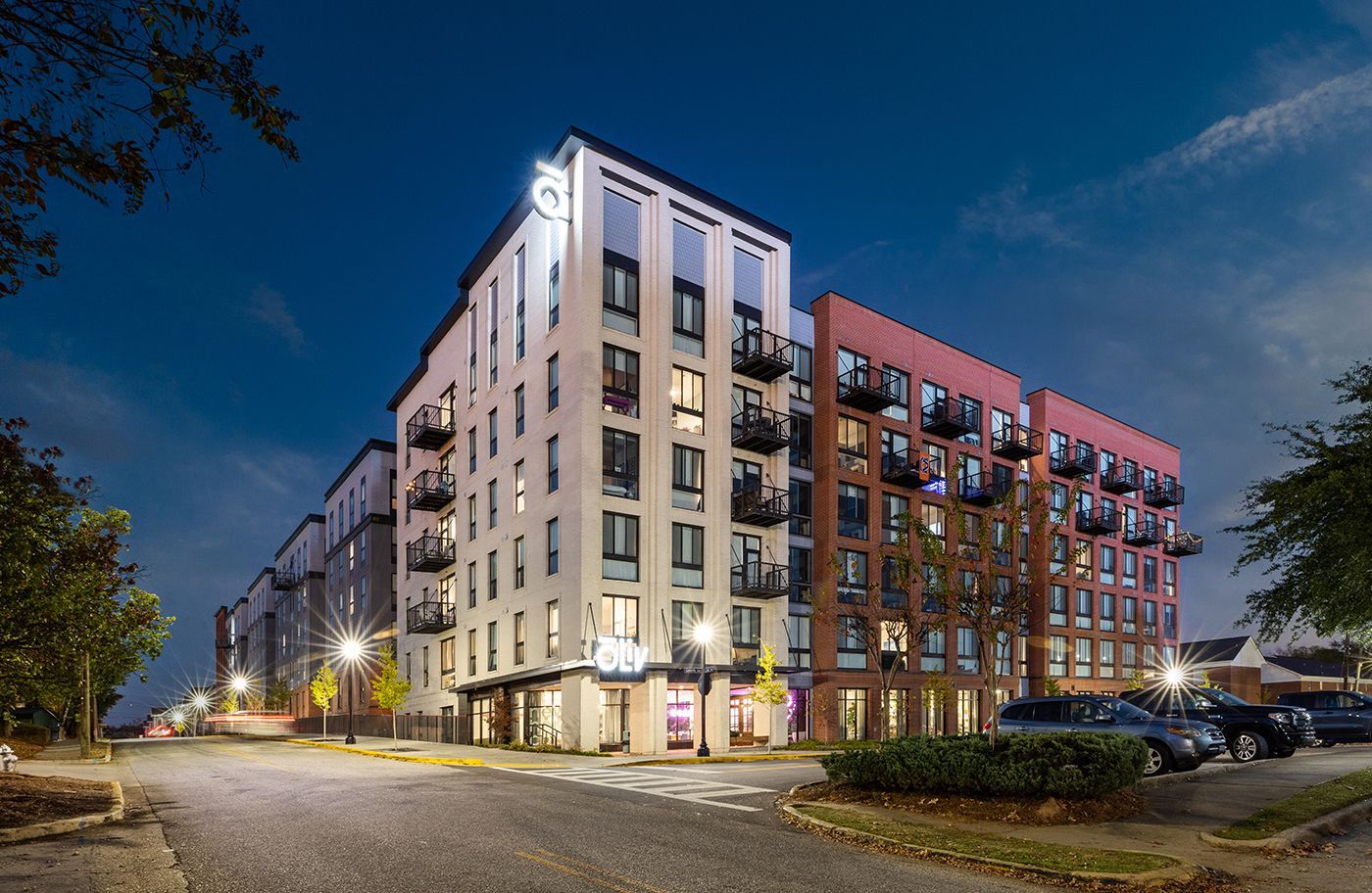 A large apartment building with cars parked in front of it at night.