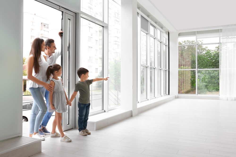 Family entering an empty new home, son pointing toward floor-to-ceiling windows.