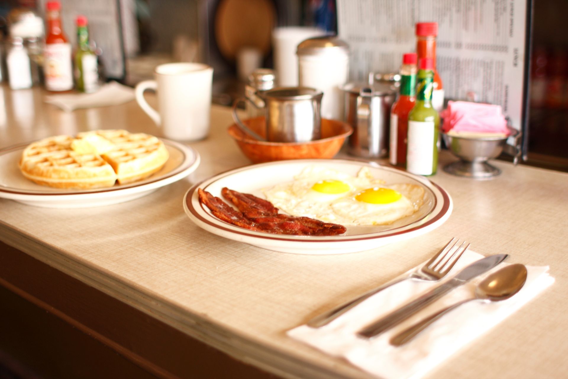 A table with plates of food including eggs bacon and waffles