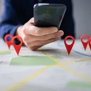 Hand holding smartphone over a map with red location pins marking places