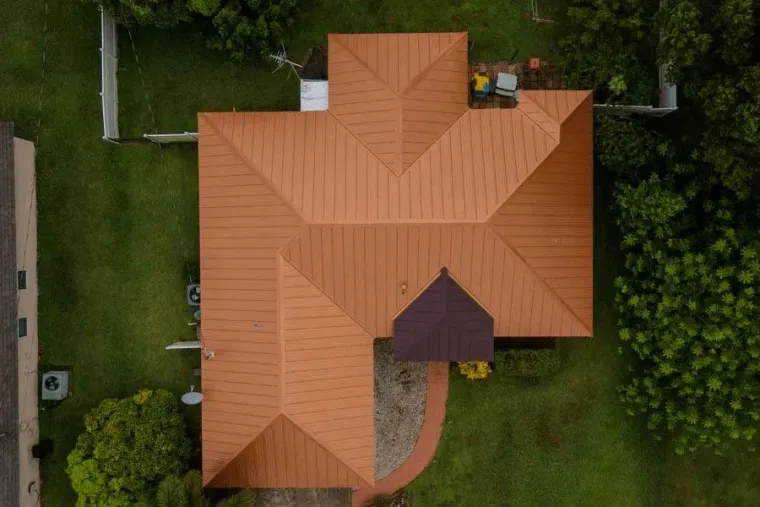Aerial view of a house with an orange roof surrounded by green lawn and trees.
