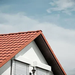 Red-tiled house roof with white gable and wall lantern against a cloudy sky
