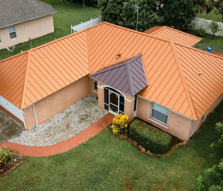 Aerial view of a tan house with an orange metal roof and a small front entrance porch