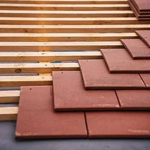 Partially installed terracotta roof tiles over wooden battens
