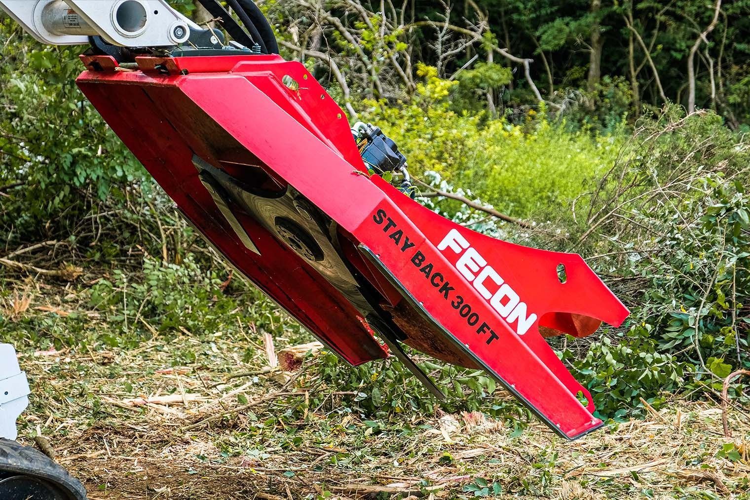Red FCON brush cutter attached to a machine clearing overgrown vegetation.